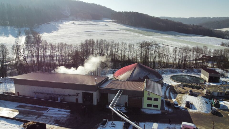 Luftaufnahme der ökologischen Klärschlammtrocknungsanlage in Offenhausen mit aufsteigendem Dampf vom Dach, umgeben von schneebedeckter Landschaft und bewaldeten Hügeln.